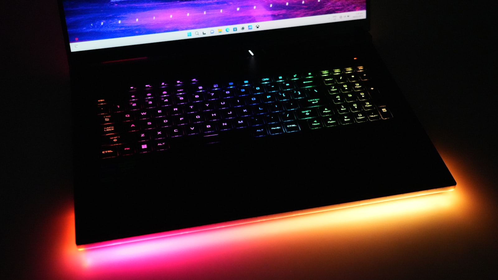 A gaming laptop with a colourful RGB backlit keyboard in a dark room